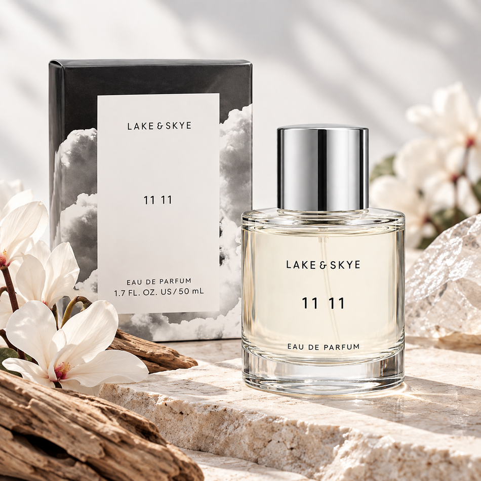 Lake & Skye 11 11 Eau de Parfum 1.7 oz 50 mL perfume bottle with silver cap and original cloud-design packaging displayed on a natural stone surface with white flowers, driftwood, and a serene coastal background.